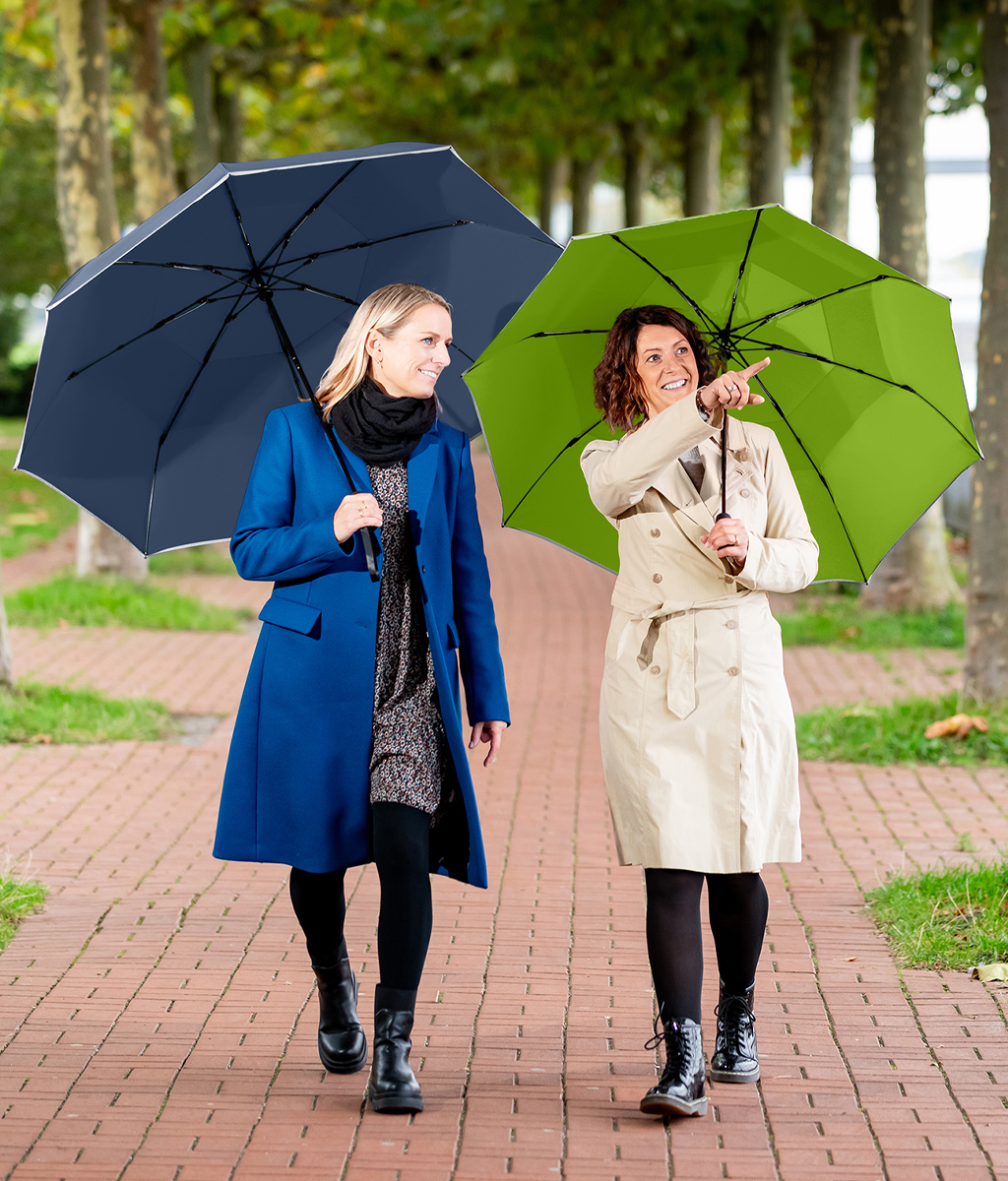 Two women with umbrellas are walking along an alley of trees.