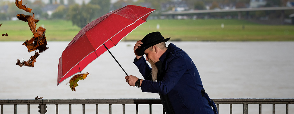 Mann mit Hut kämpft mit Regenschirm gegen den Wind an