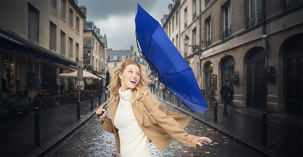 Blauer windproof Regenschirm der Marke FARE im Härtetest bei Sturm und Regen in der Stadt, gehalten von einer jungen Frau