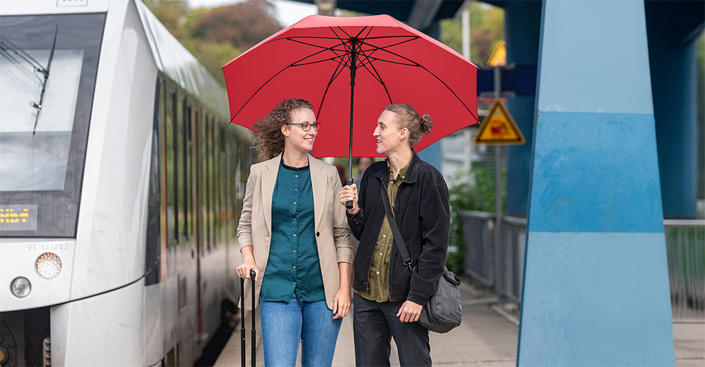Paar an einem Bahnhof unter einem großen Schirm