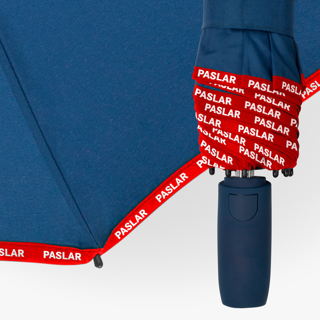 Nahaufnahme eines dunkelblauen Taschenschirms mit grüner Paspelierung entlang der Bezugskanten. Auch das Schließband ist grün und mit dem Schriftzug „ALPINA“ versehen, der Griff ist in Dunkelblau gehalten.