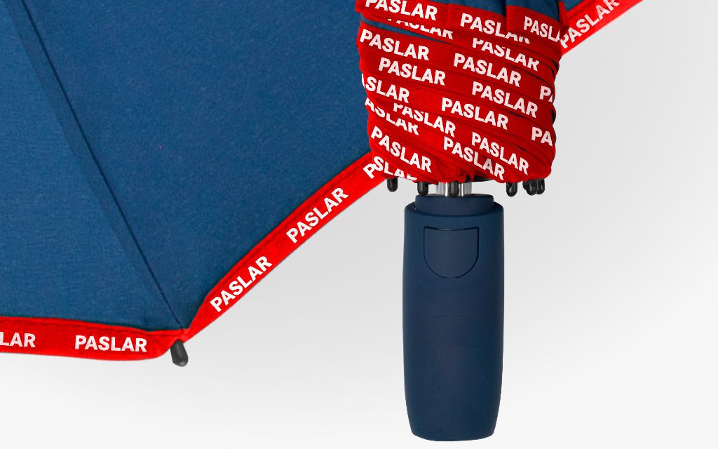 Blauer Taschenschirm mit roter PASLAR-Paspelierung und dunkelblauem Griff.