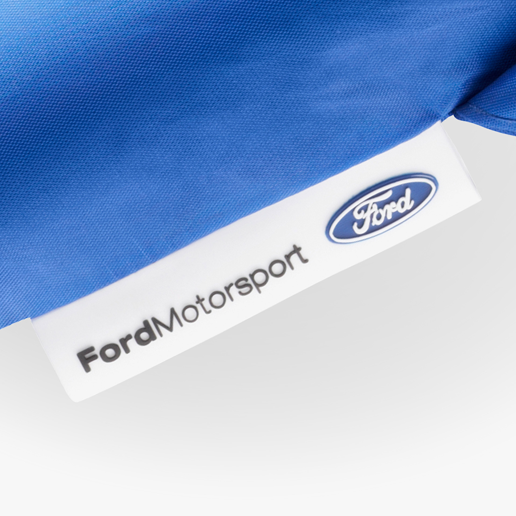 Nahaufnahme eines blauen Schirms mit angebrachtem weißem Patch am Saum. Auf dem Patch sind der Schriftzug „Ford Motorsport“ sowie das blaue Ford-Logo zu sehen.