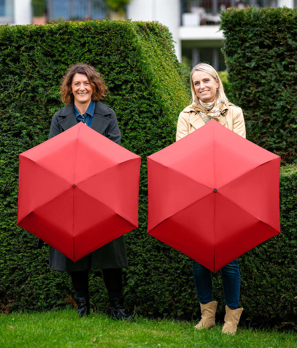 Two women with pocket umbrellas in front of a hedge